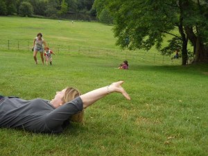 A woman rolling down a grassy hill. Families are playing on the grass in the background.